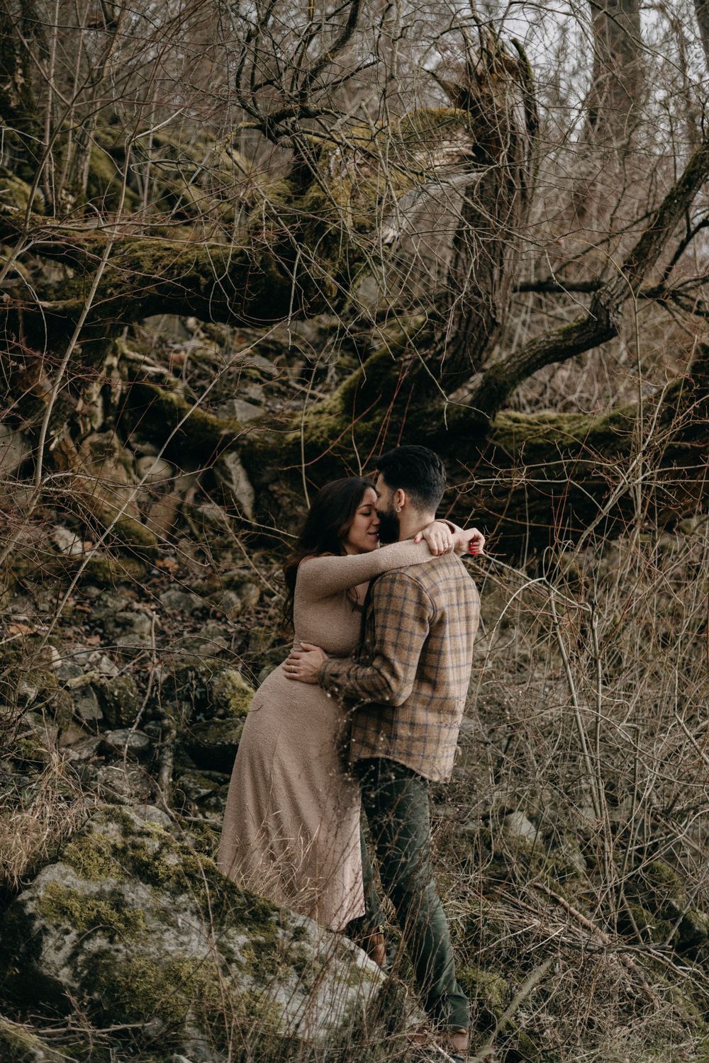 Romantic maternity photo of couple embracing against rugged winter landscape.