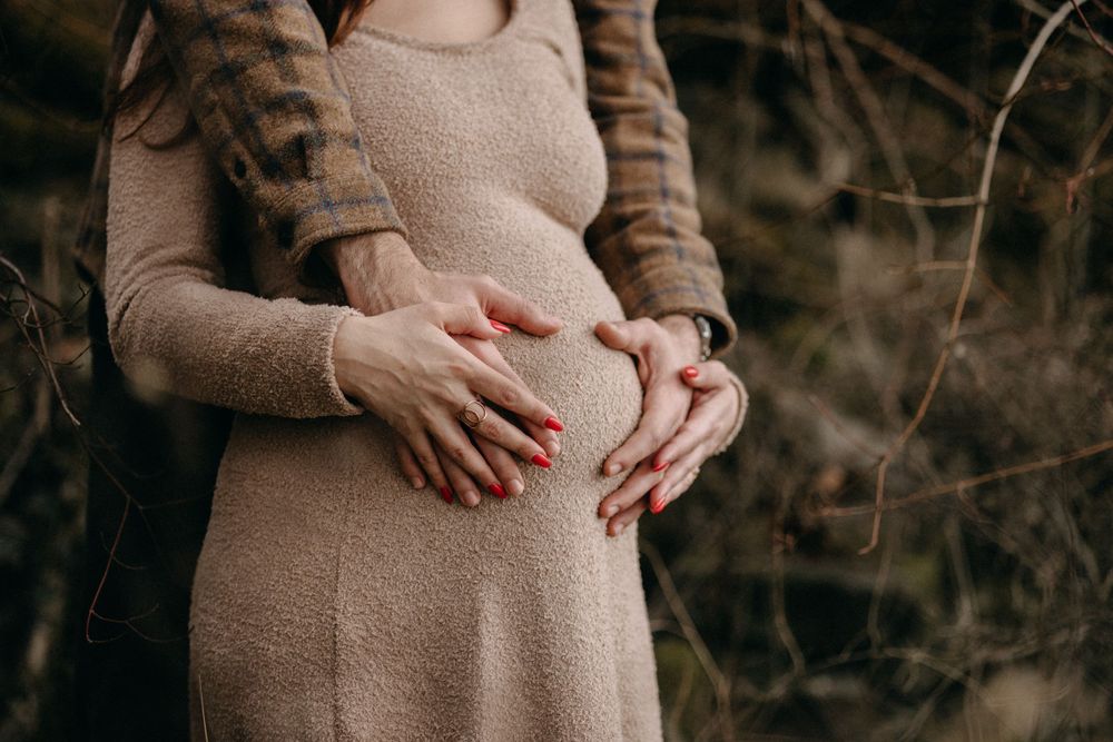 Close-up of hands cradling a pregnant belly in a beige knit dress.