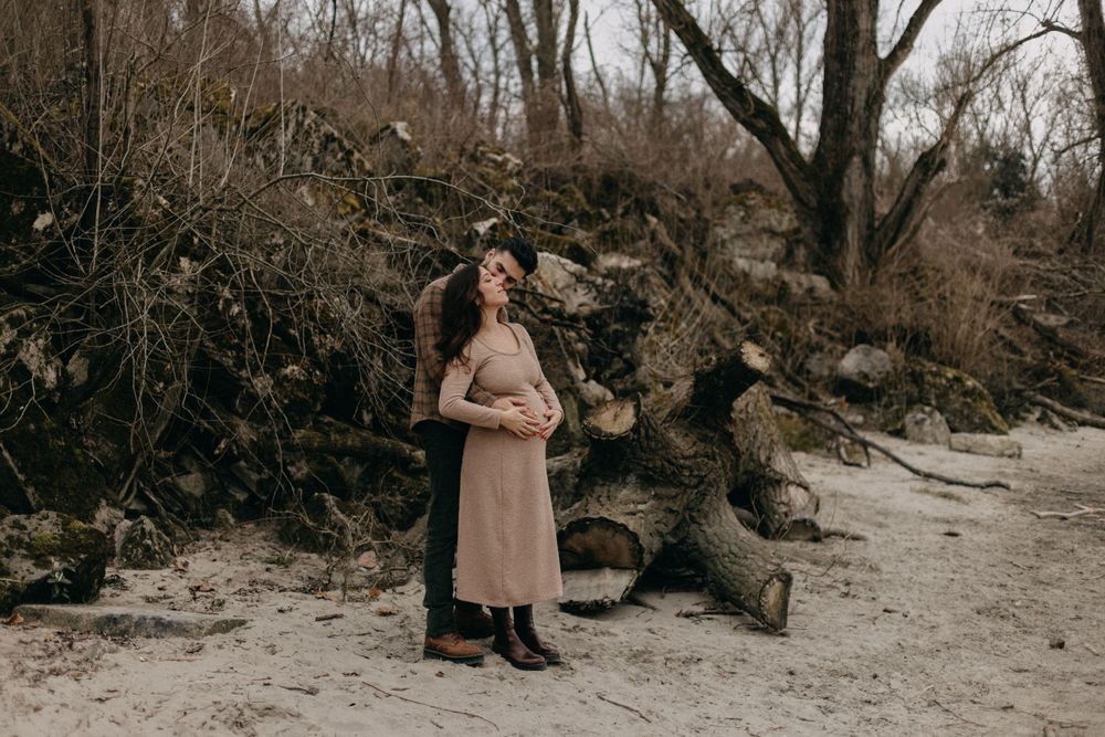 Expecting couple shares tender moment in winter landscape with fallen logs.