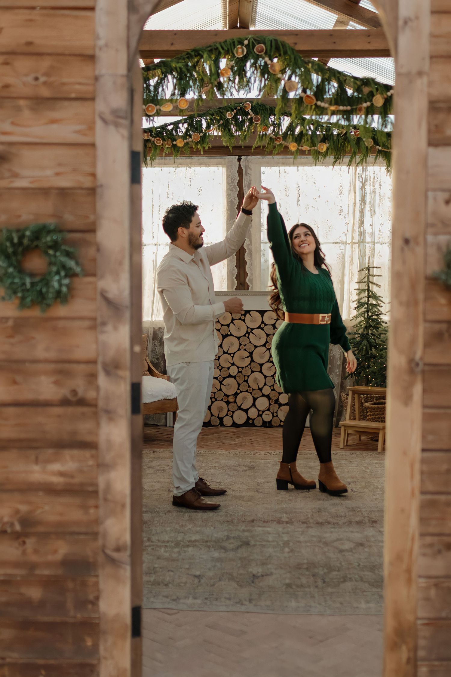 Two people in festive attire enjoying a moment together in a rustic wooden cabin decorated with holiday greenery.