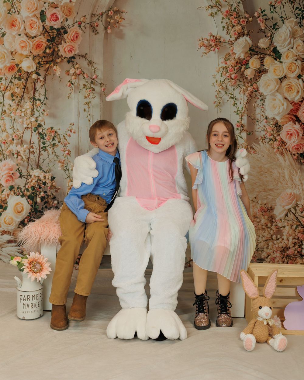 Easter scene with a large white bunny character posing with children against a floral backdrop with peach and pink flowers.