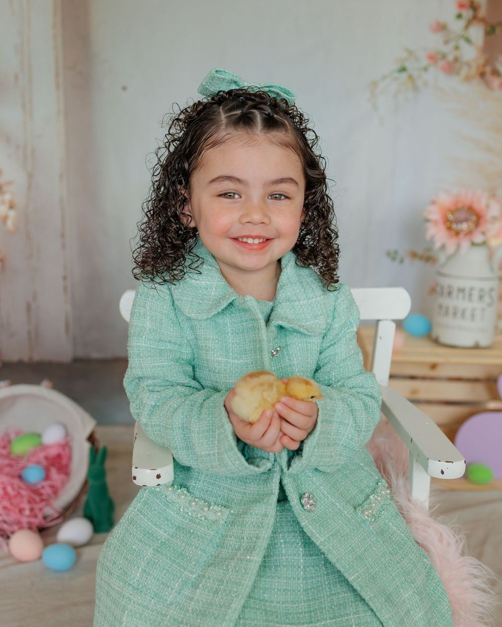 A child in a mint green tweed outfit sits at a styled Easter table setting with pastel decorations and Easter eggs.