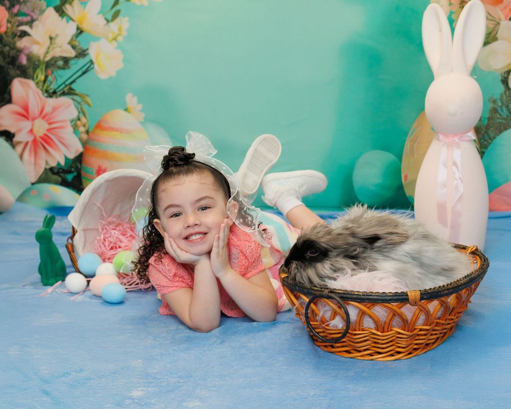 Easter themed photo setup with wicker basket, bunny decorations, floral backdrop and blue floor covering.