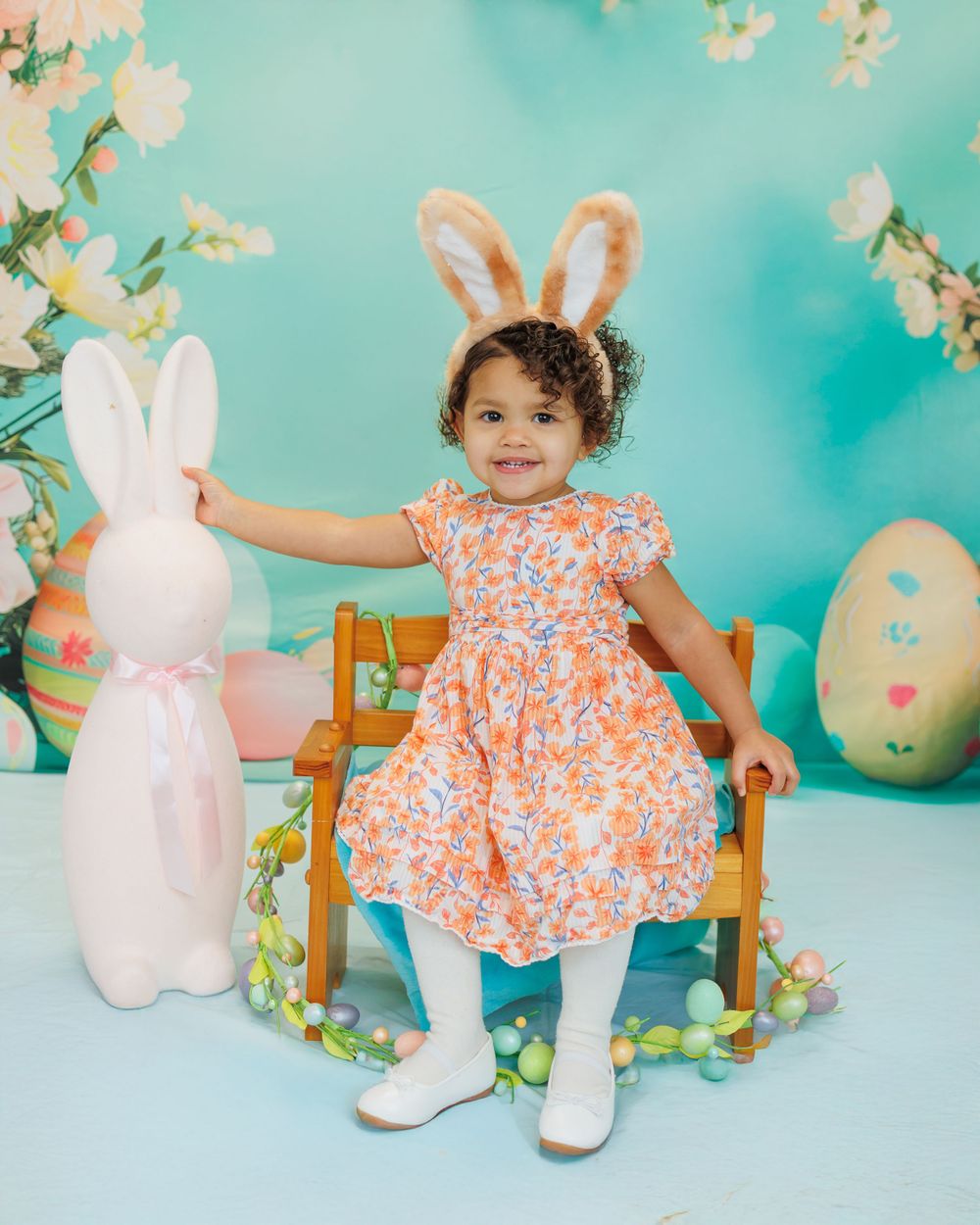 Easter scene with bunny ears, floral dress, and decorative elements against turquoise background with cherry blossoms.