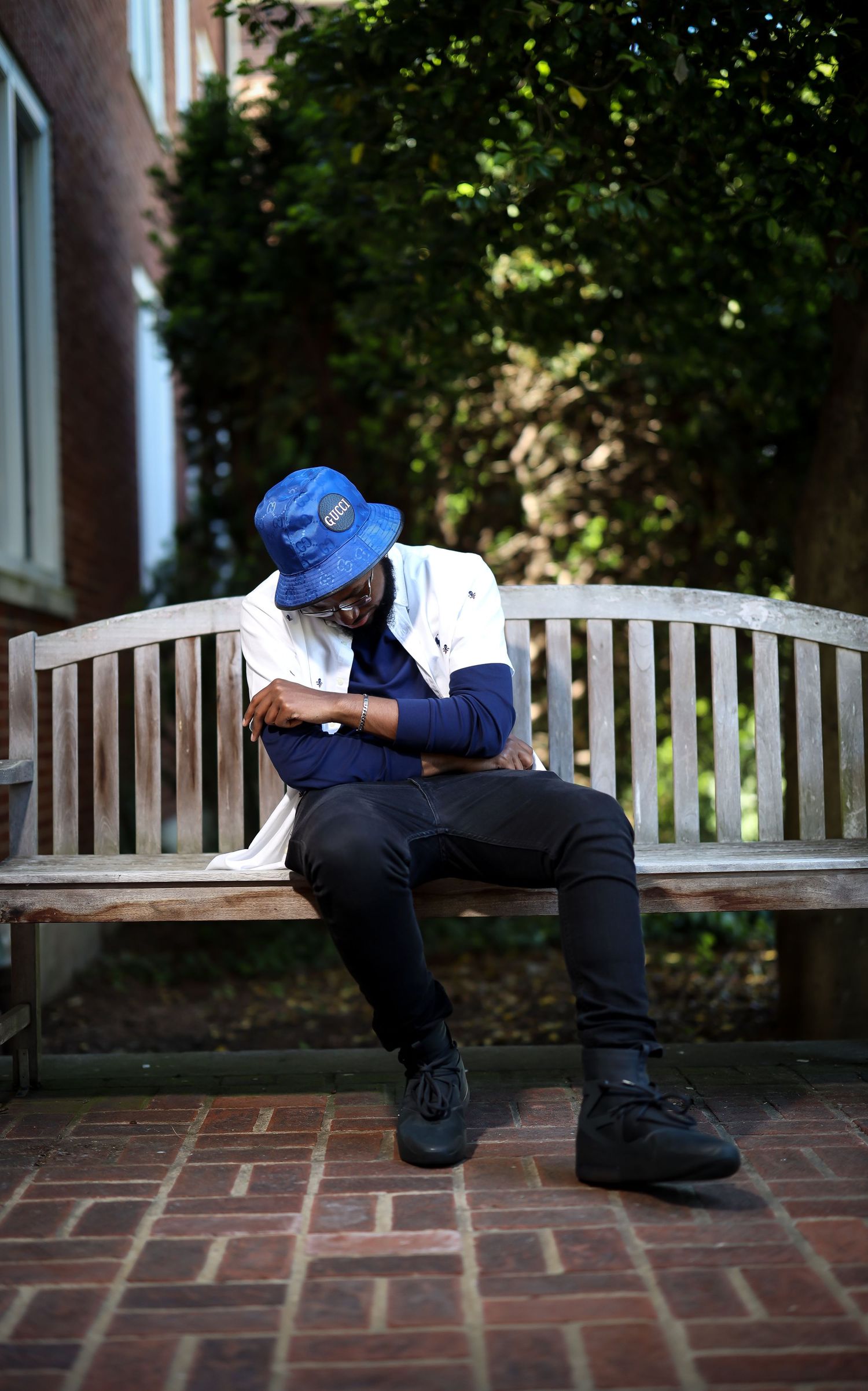 Person wearing a blue cap and white jacket sitting on a wooden bench in an outdoor setting.
