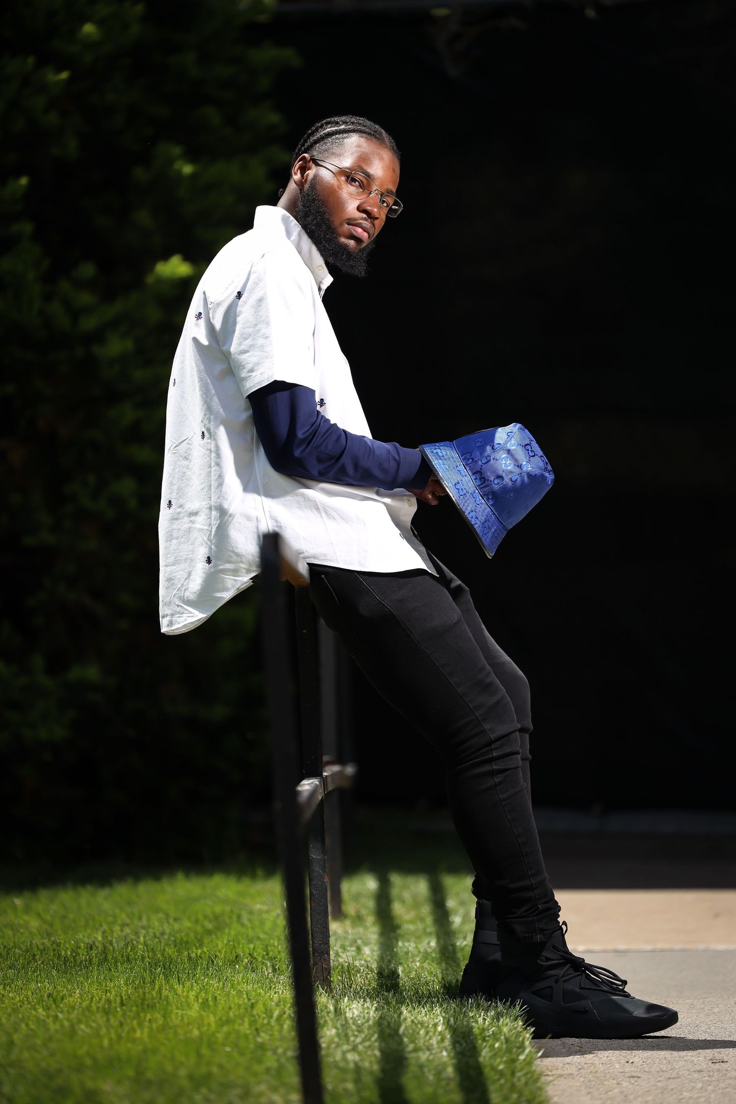 Person in white jacket and navy layers posing against outdoor railing with dramatic lighting.