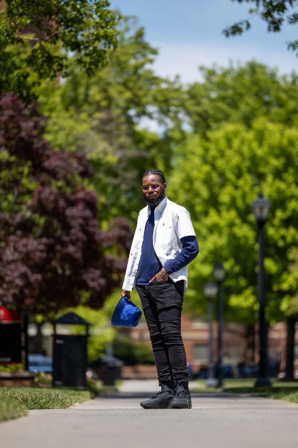 Person in white jacket and navy layers standing on campus pathway surrounded by spring foliage.