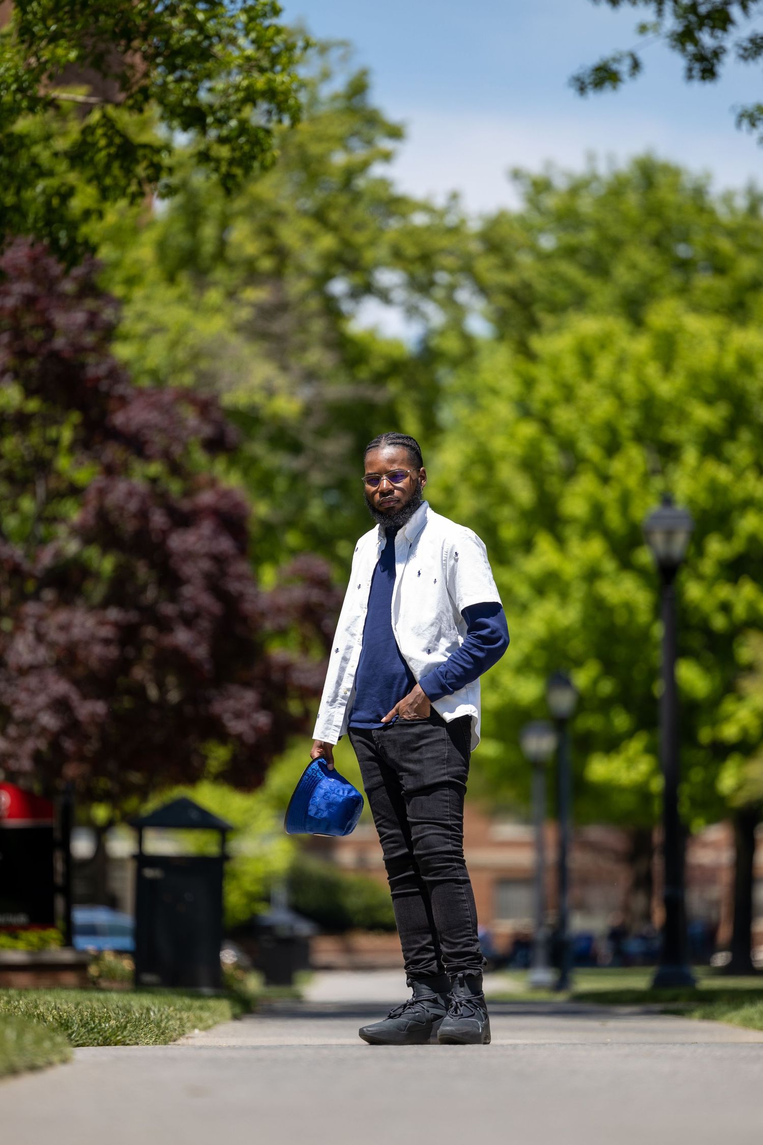 Person in white jacket and navy layers standing on campus pathway surrounded by spring foliage.