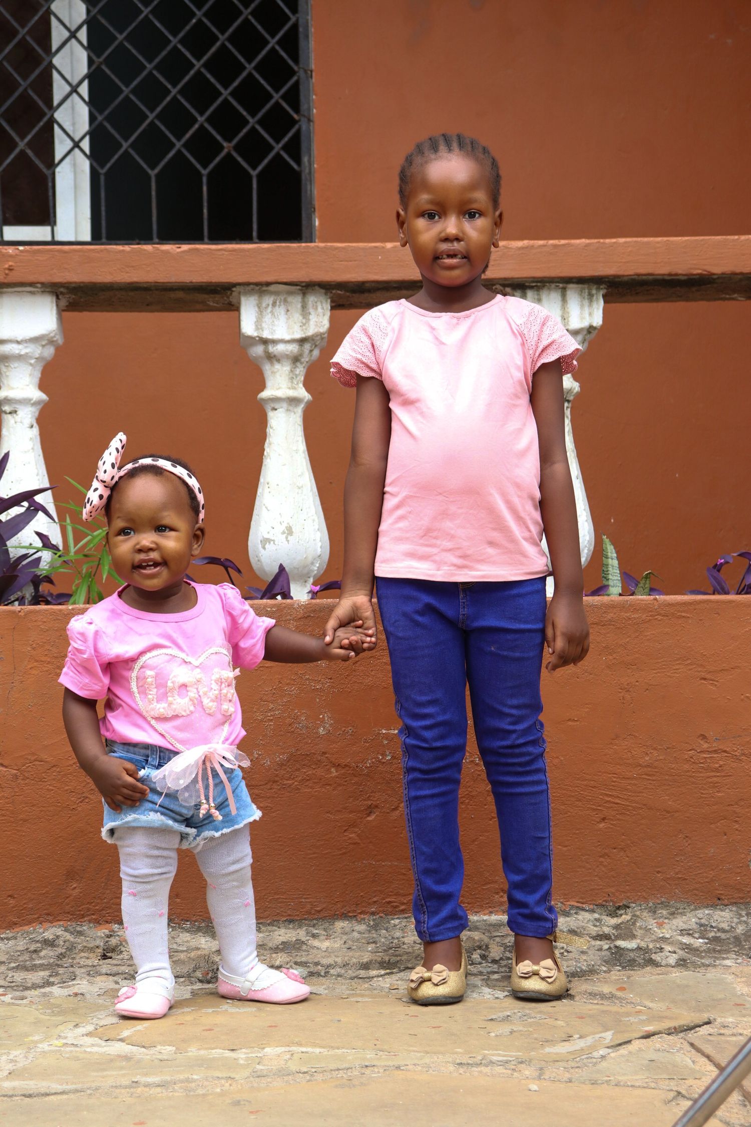 Two children holding hands in front of a balcony
