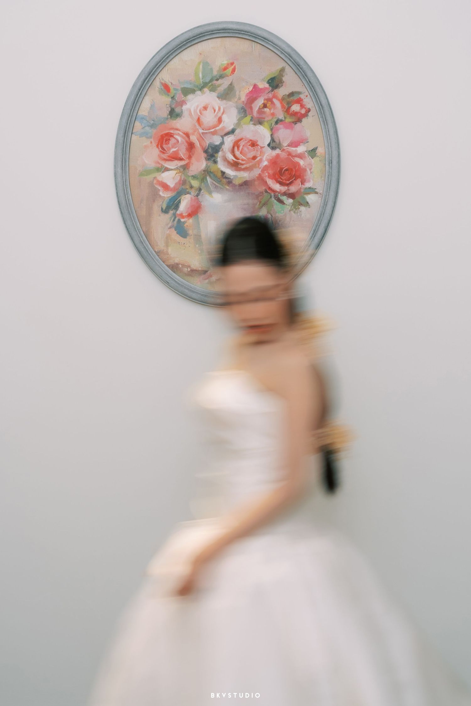 Motion-blurred figure in white dress passes vintage floral mirror in dreamy portrait.