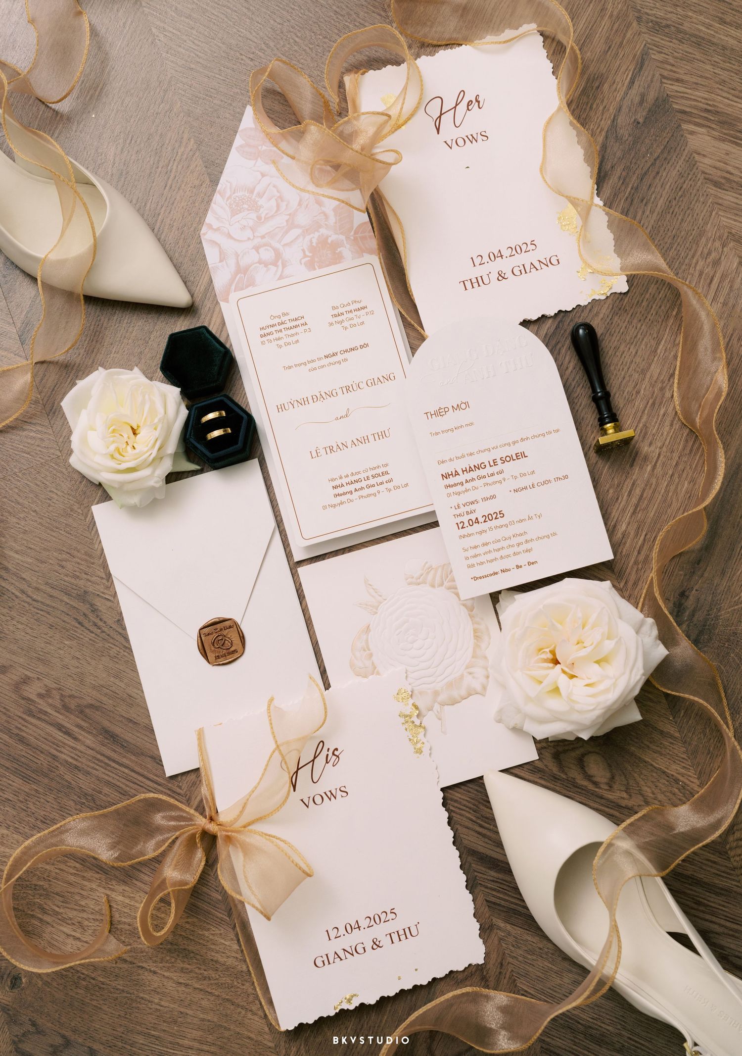Elegant wedding invitation suite in white and gold with roses, wax seal, and ribbon on wooden surface.