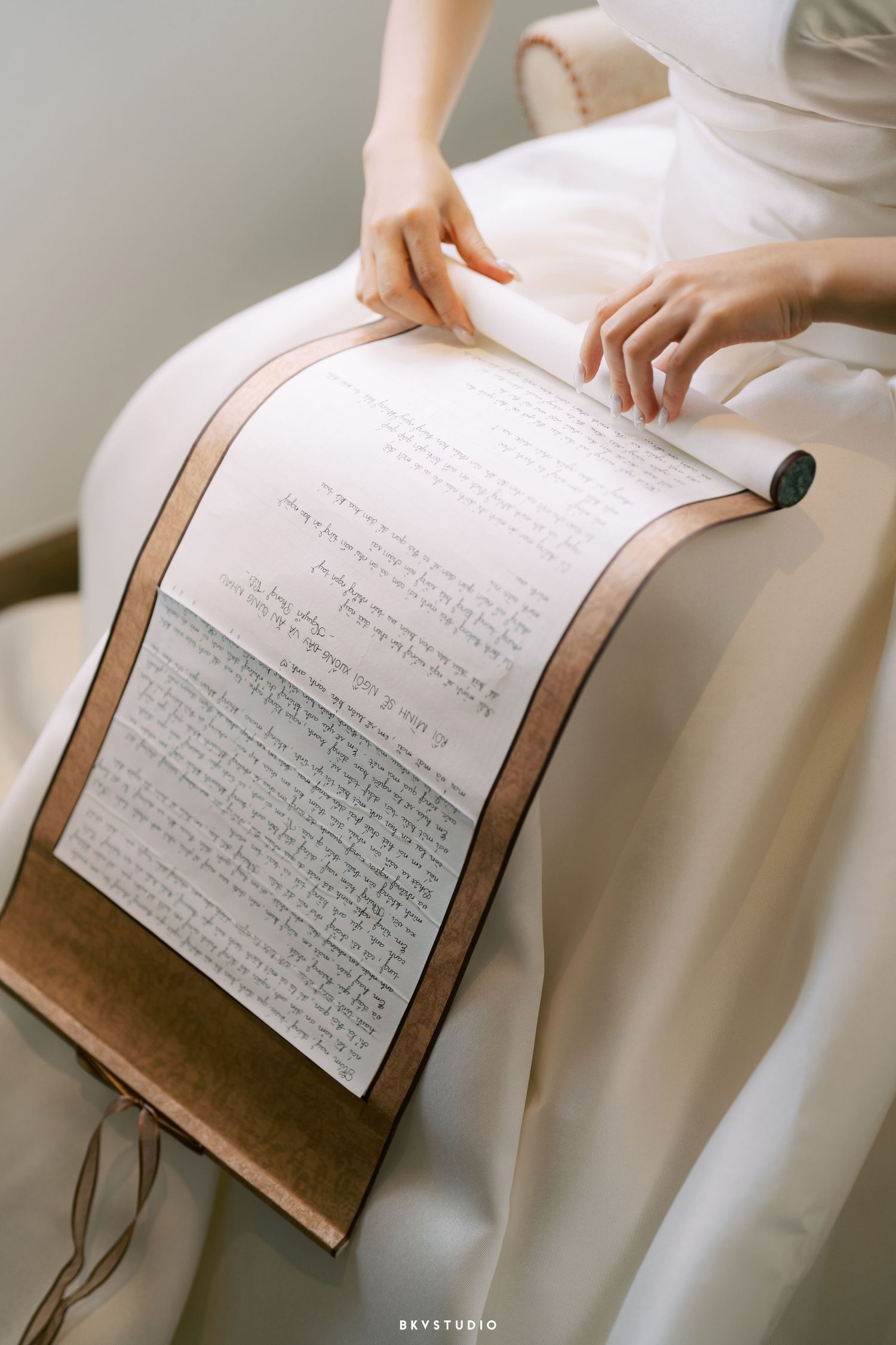Hands touch an unfolded sheet of text printed on white paper laid across a leather-bound book in a minimalist setting.