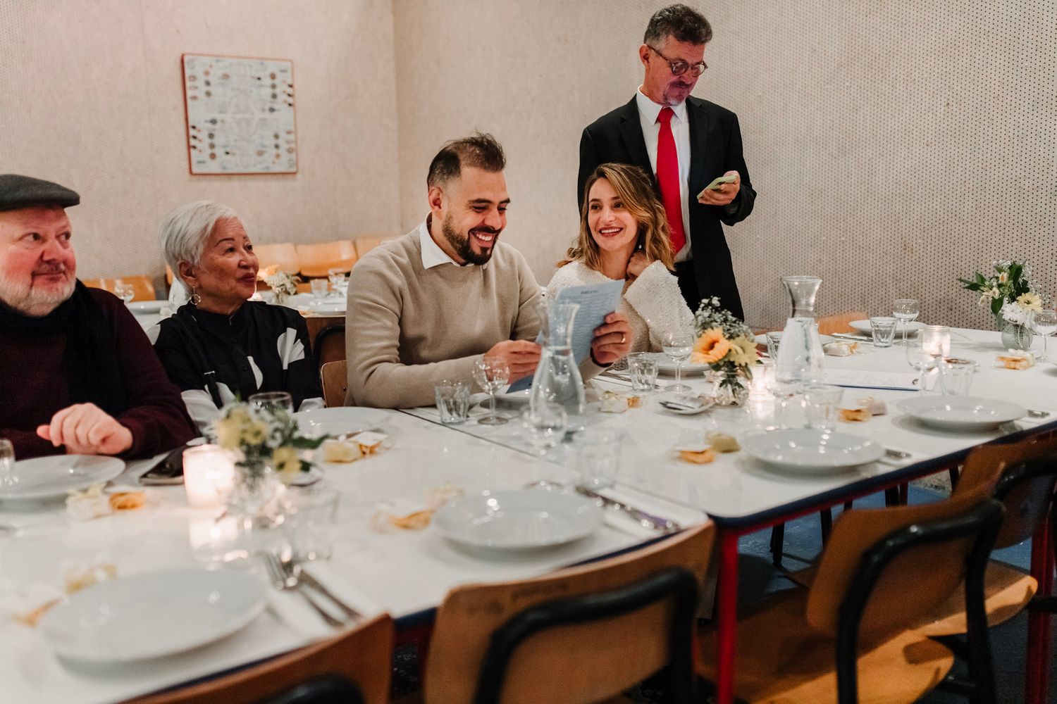 Panoramic view of a formal dining table set with white plates and floral centerpieces during a wedding celebration.
