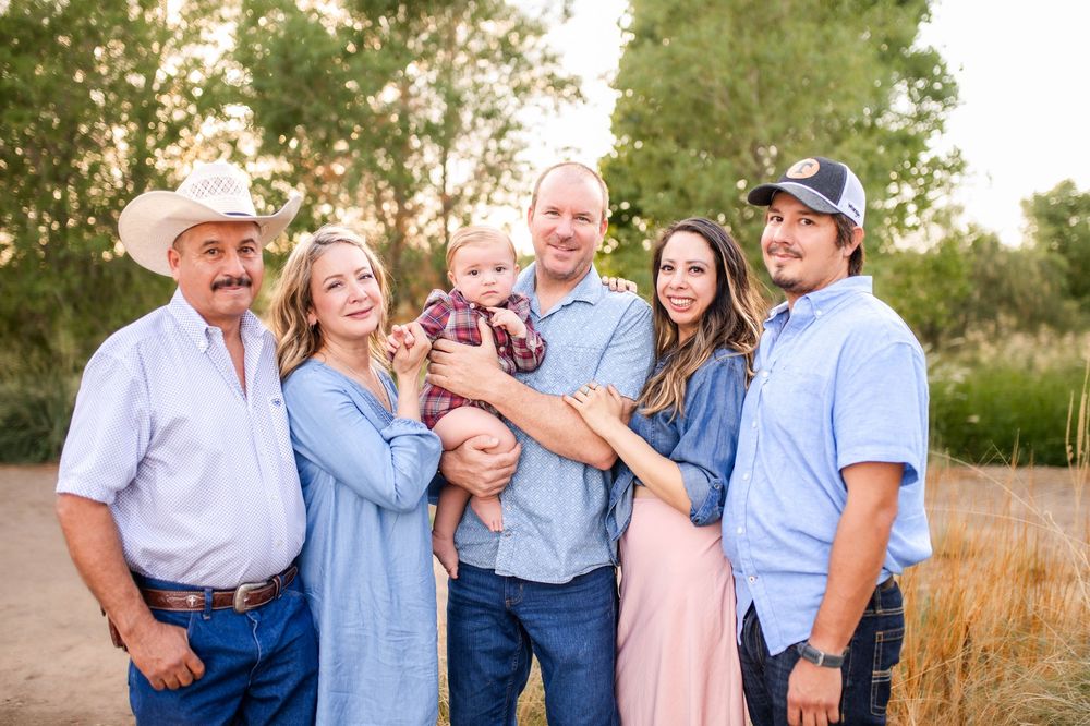 Extended family of six adults and one baby posing together outdoors in warm golden light.