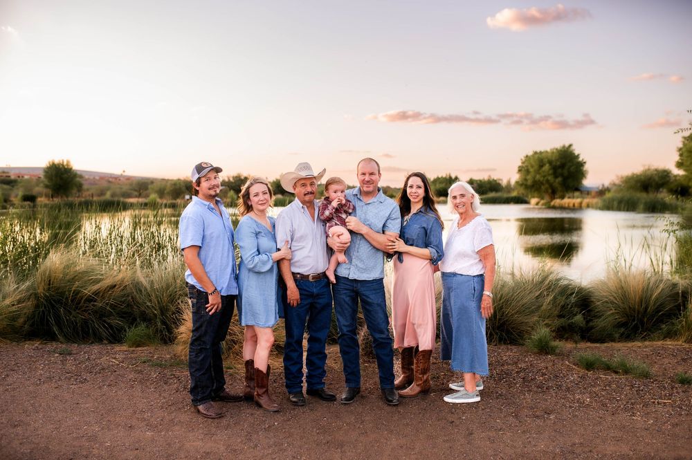 Large extended family of nine posing together near a pond at colorful sunset.