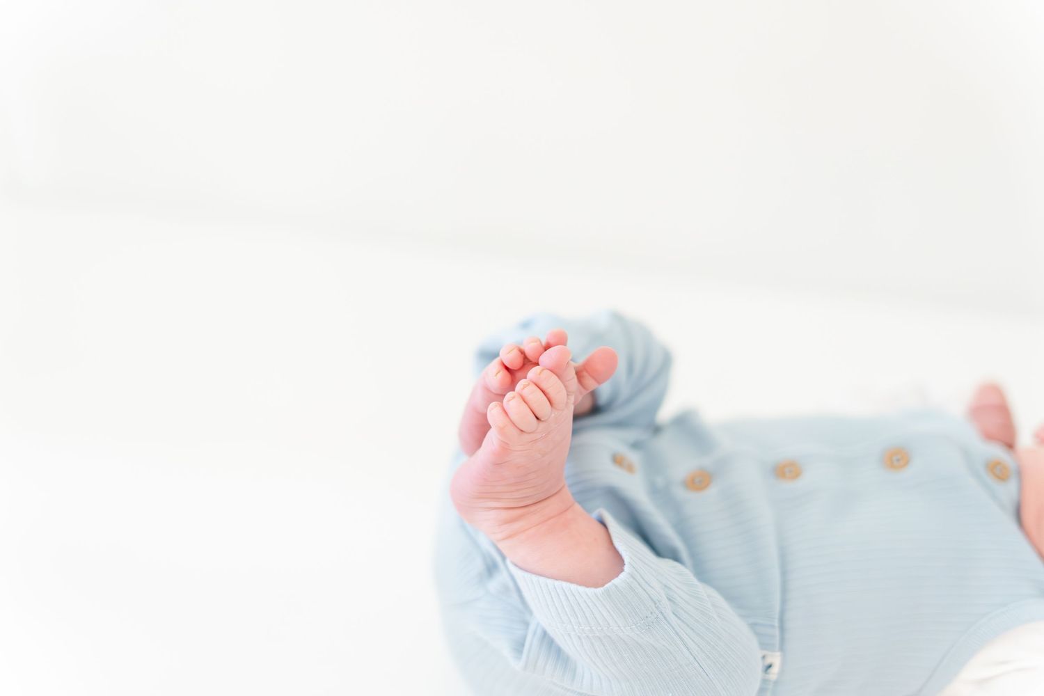 Close-up of a newborn baby's tiny feet and toes in a soft blue outfit on a white background.