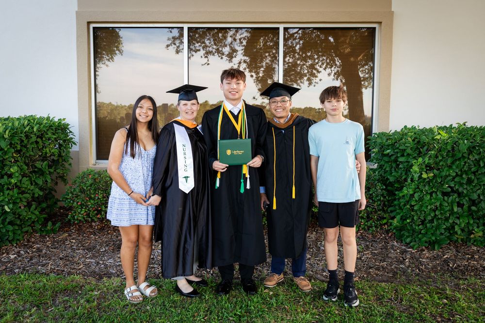 Two graduates in caps and gowns pose with family members outside after a graduation ceremony.