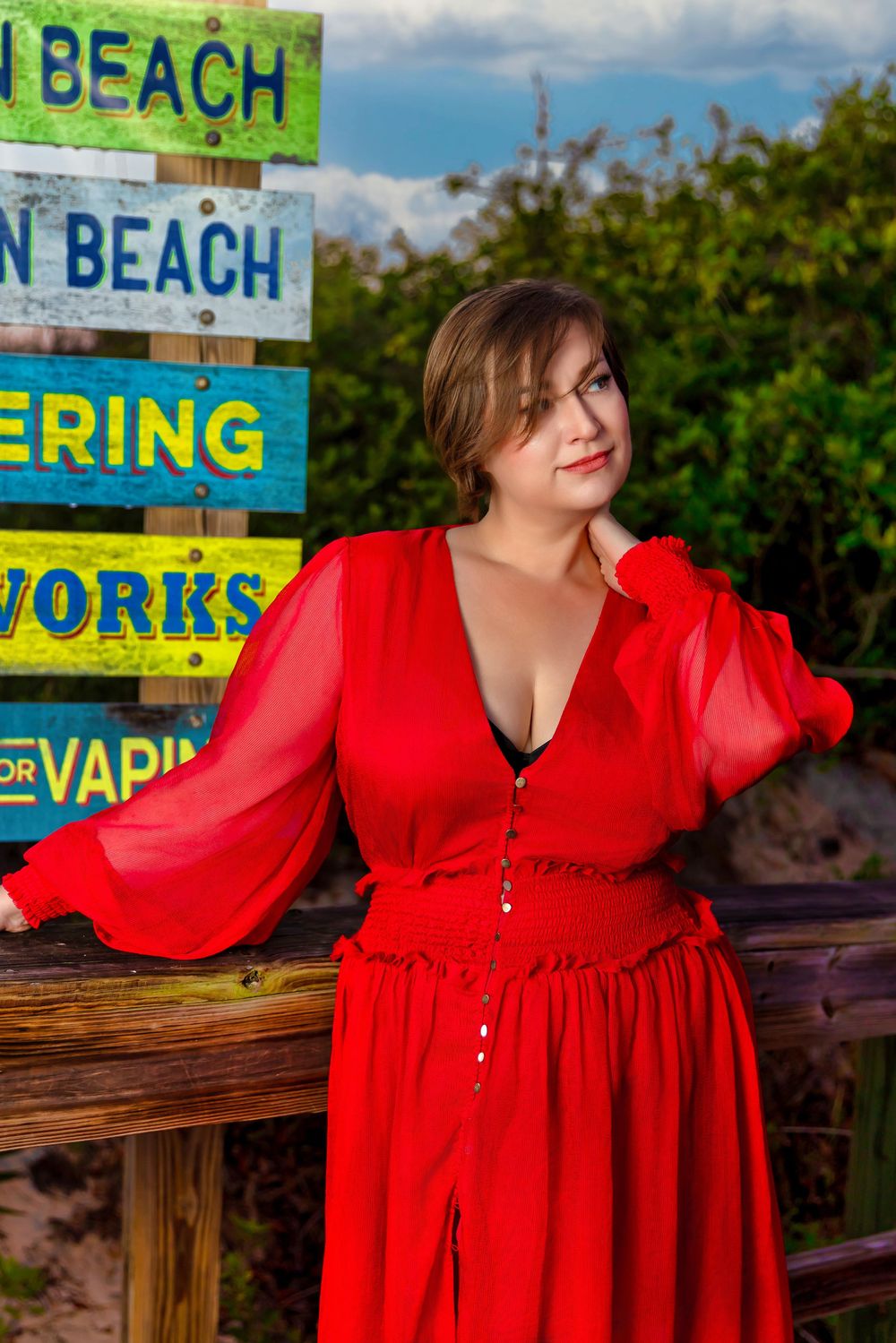 Woman in red dress poses by colorful beach signs outdoors.