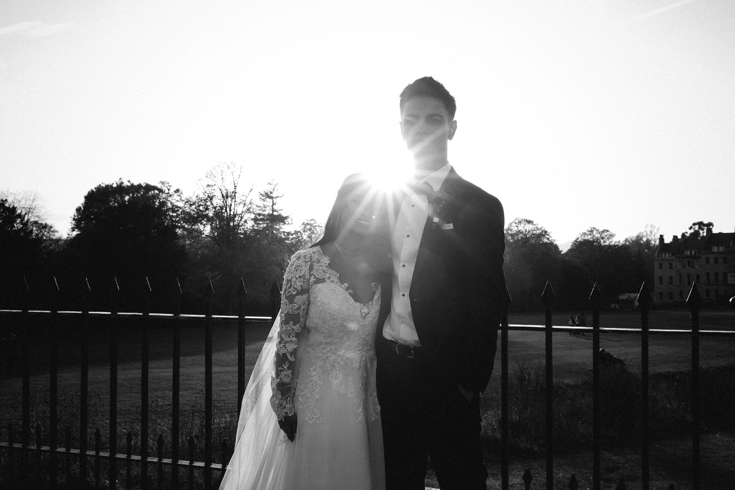 Black and white photo of a bride and groom holding hands walking through a sunlit forest clearing on their wedding day.