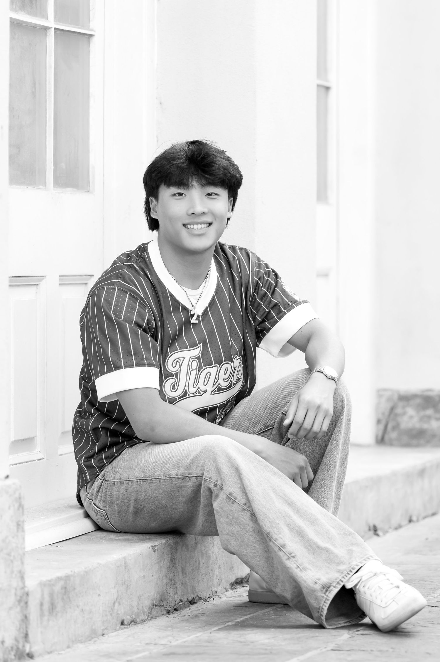 Young man in Tigers baseball jersey sitting on steps smiling in black and white portrait photo.