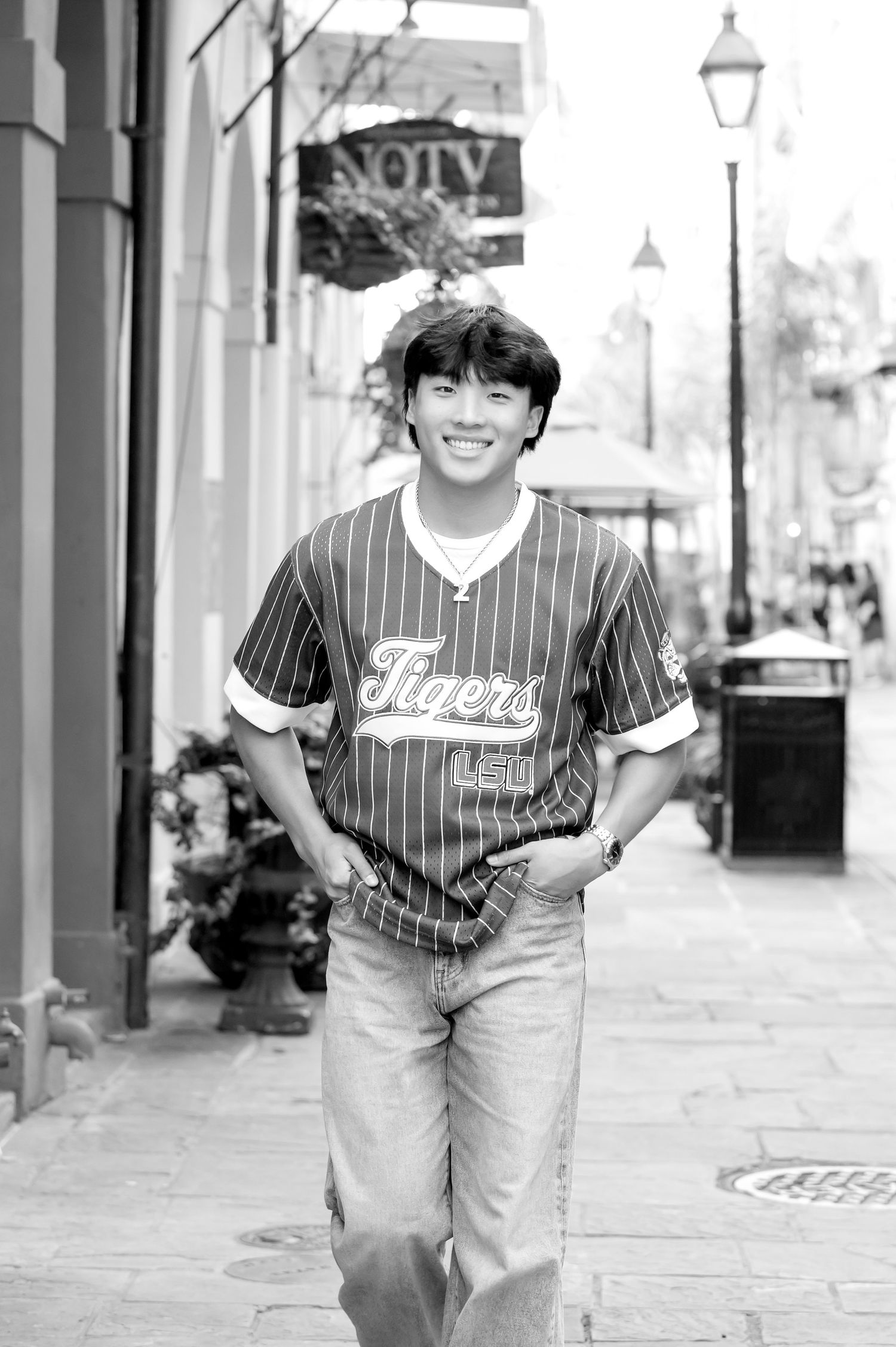 Smiling young man in LSU Tigers baseball jersey and jeans walking on a city sidewalk in black and white photo.