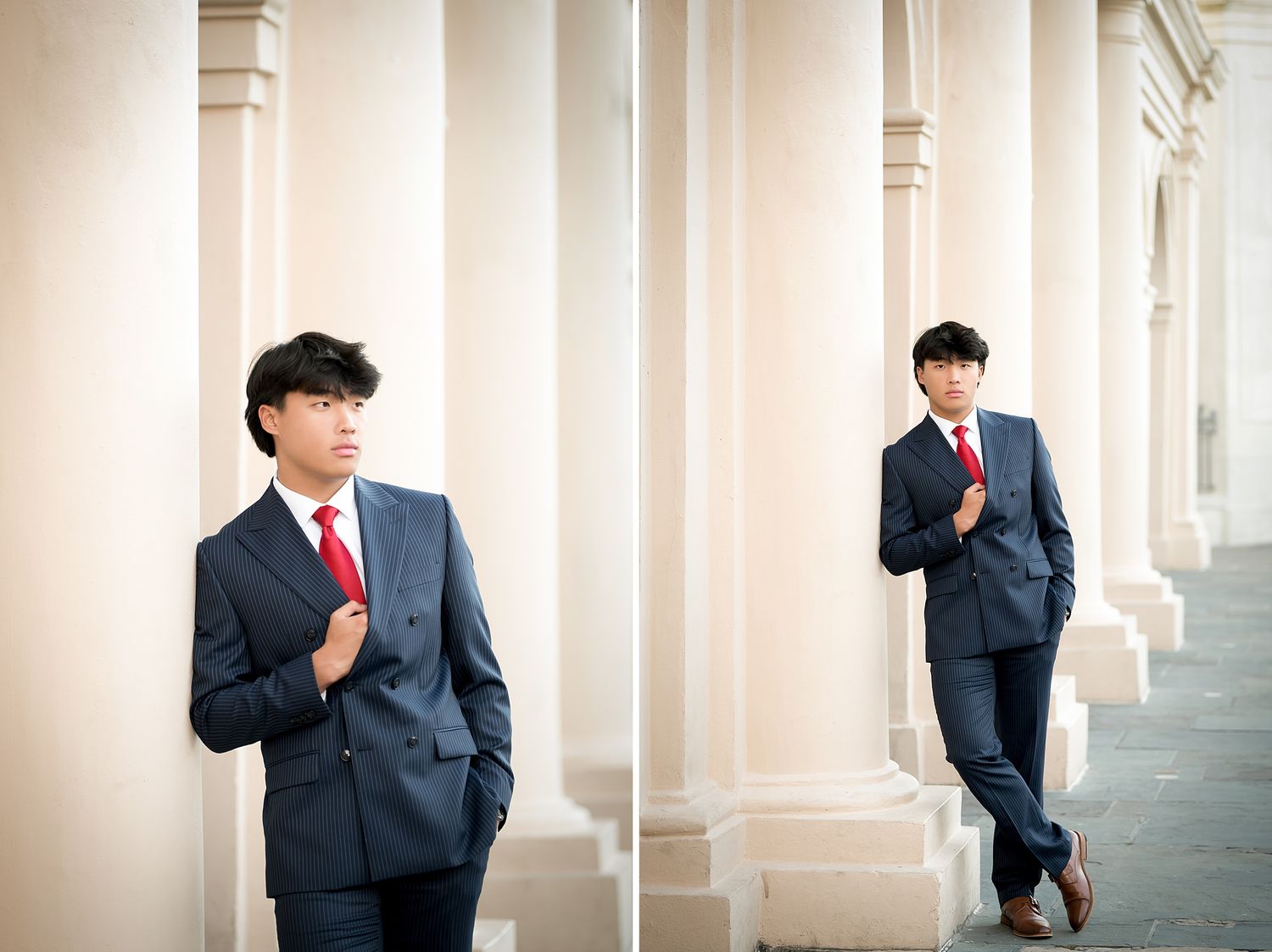 Young man in navy suit with red tie poses confidently between white columns for senior portrait photos.