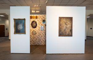 Art gallery installation with vintage-style paintings displayed on white walls and floral wallpaper backdrop.