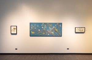 Gallery wall displaying three botanical artworks, with a large blue horizontal piece as the centerpiece.