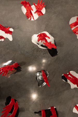 Red and white sculptural hand forms scattered across a grey concrete gallery floor.