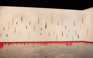 Dark vertical rods with red dripping paint installation on a white gallery wall.