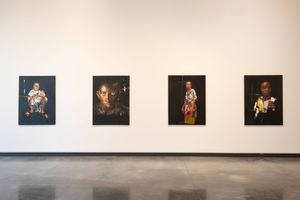 Four dark-framed portrait paintings displayed on a white gallery wall showcasing diverse subjects in colorful attire.