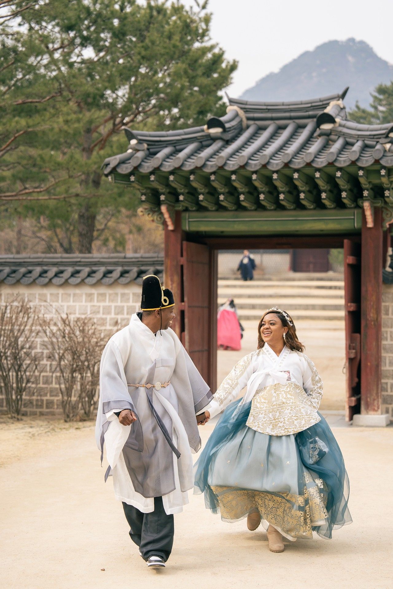 Couple in traditional Korean hanbok attire walking hand in hand at Gyeongbokgung Palace, Seoul.