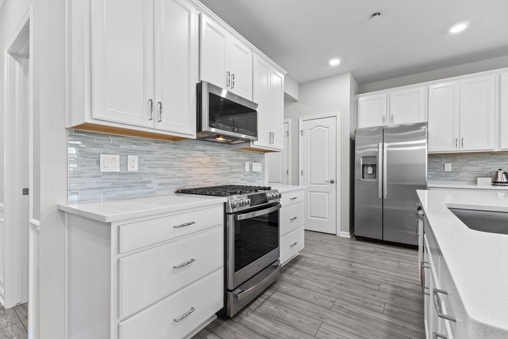 Modern white kitchen with stainless steel appliances, subway tile backsplash, and quartz countertops.