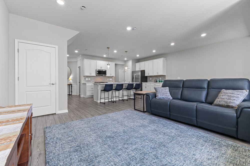 Open concept living room with blue sectional sofa, recessed lighting, and modern kitchen beyond.