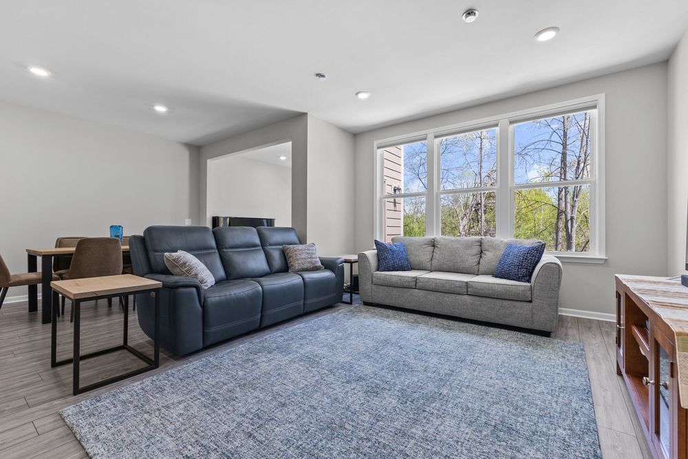 Open living room with navy blue reclining sofa, gray couch, blue area rug, and large bright windows.