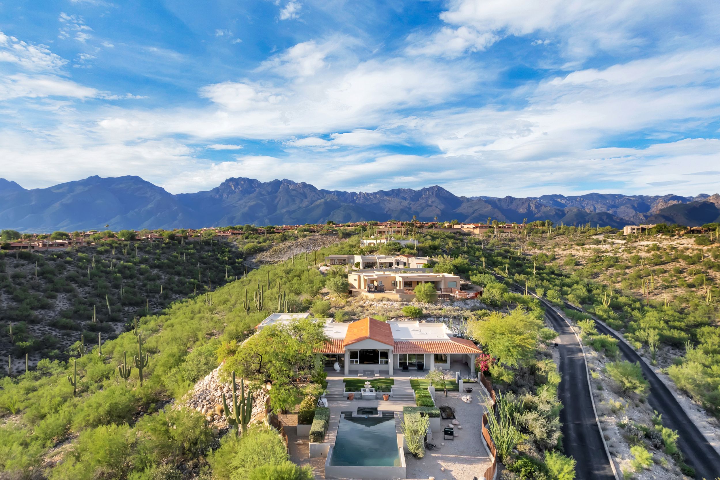 Aerial view of a luxury desert estate with a pool, surrounded by lush desert vegetation and stunning mountain backdrop.