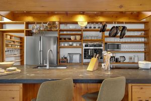 Modern kitchen interior with wood cabinets, stainless steel appliances, and open shelving displaying glassware.