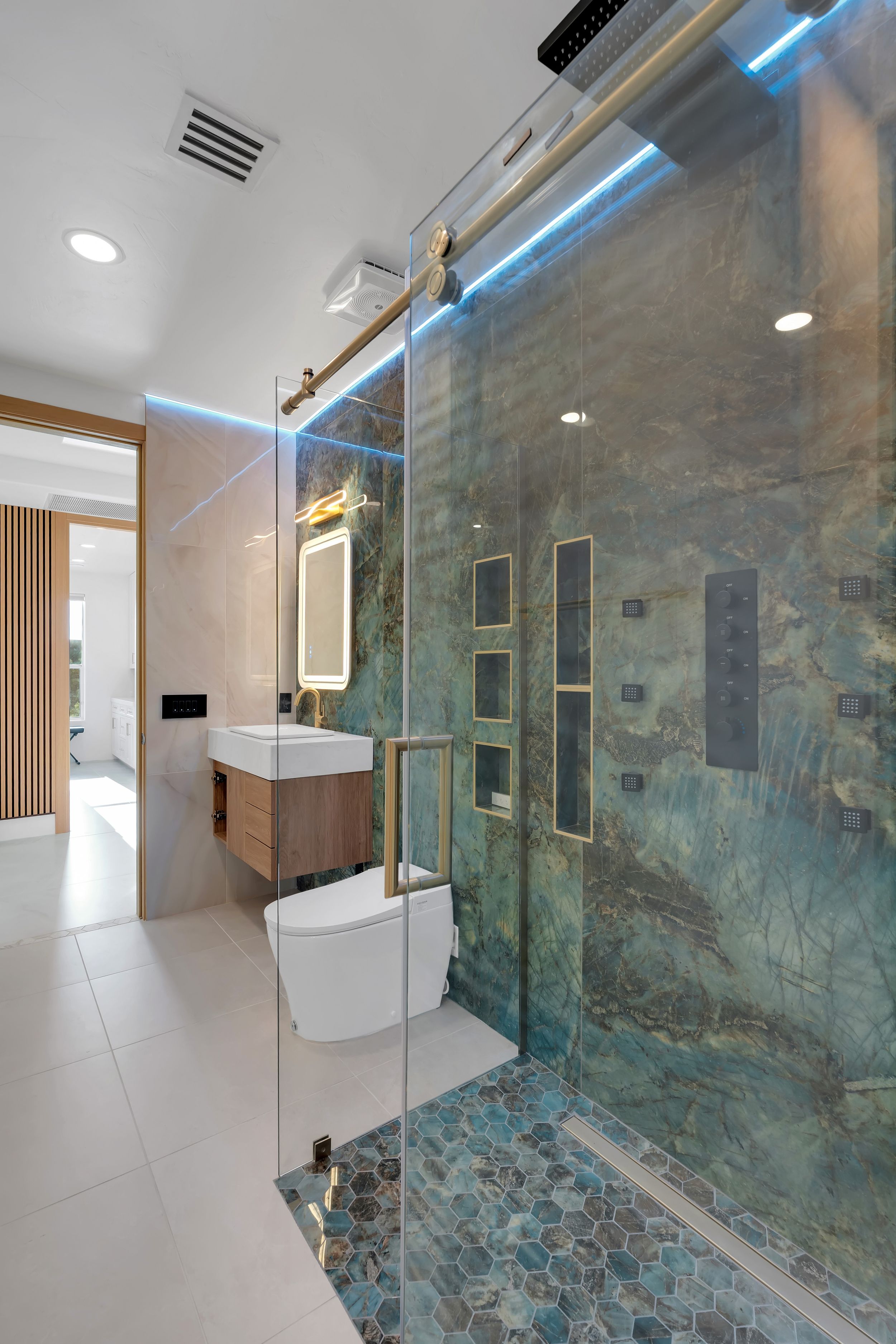 Modern luxury bathroom with blue LED lighting, green marble shower, hexagonal floor tiles, and floating wood vanity.