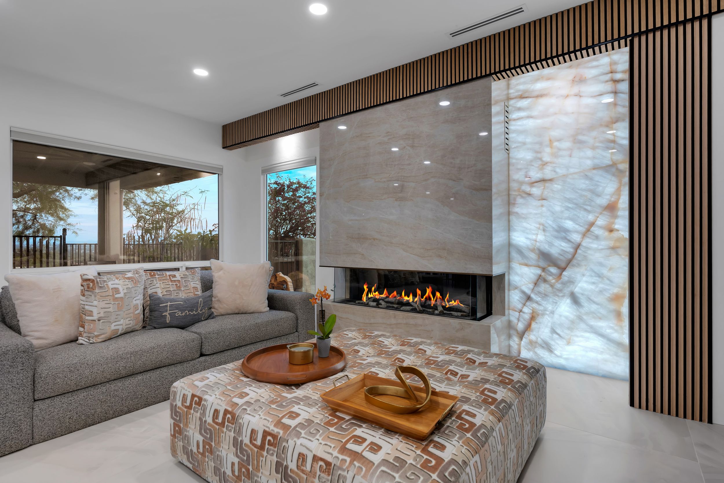 Modern living room with gray sofa, patterned ottoman, linear fireplace, and floor-to-ceiling stone accent wall.