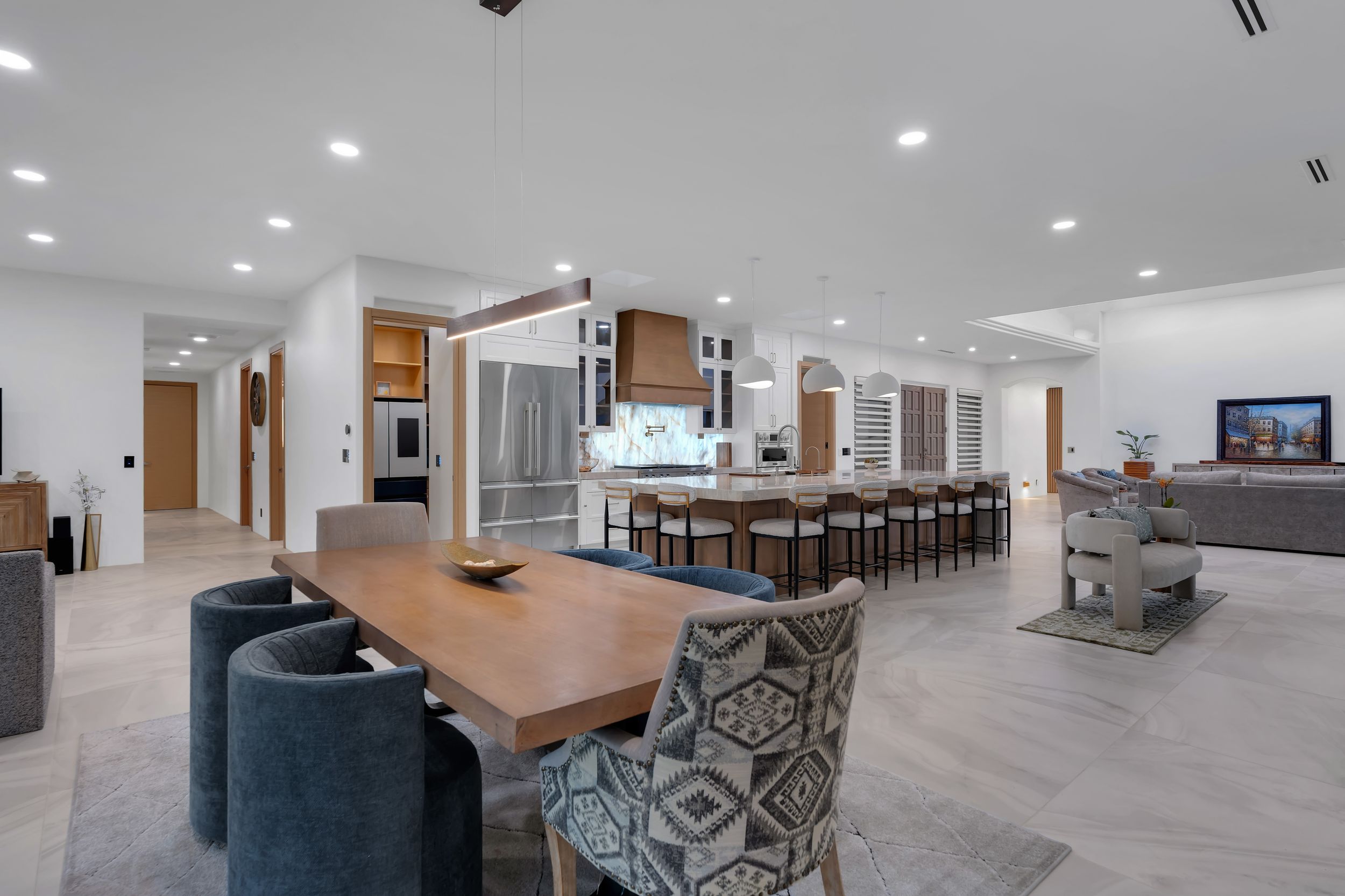 Open-concept modern kitchen and dining area with wood table, gray chairs, large island, and stainless steel appliances.