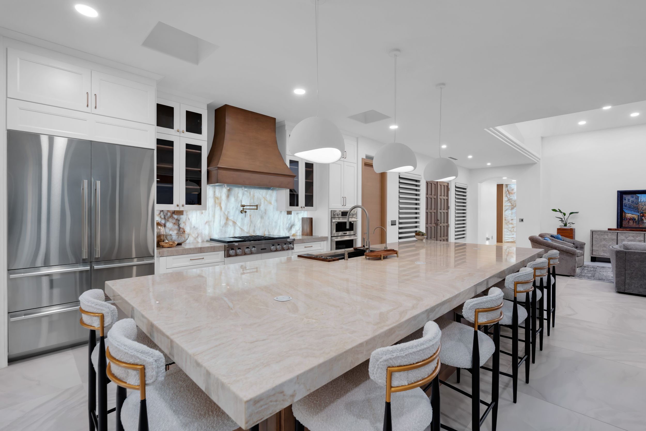 Luxurious open-concept kitchen with large marble island, bar seating, copper range hood, white cabinets, and stainless steel appliances.