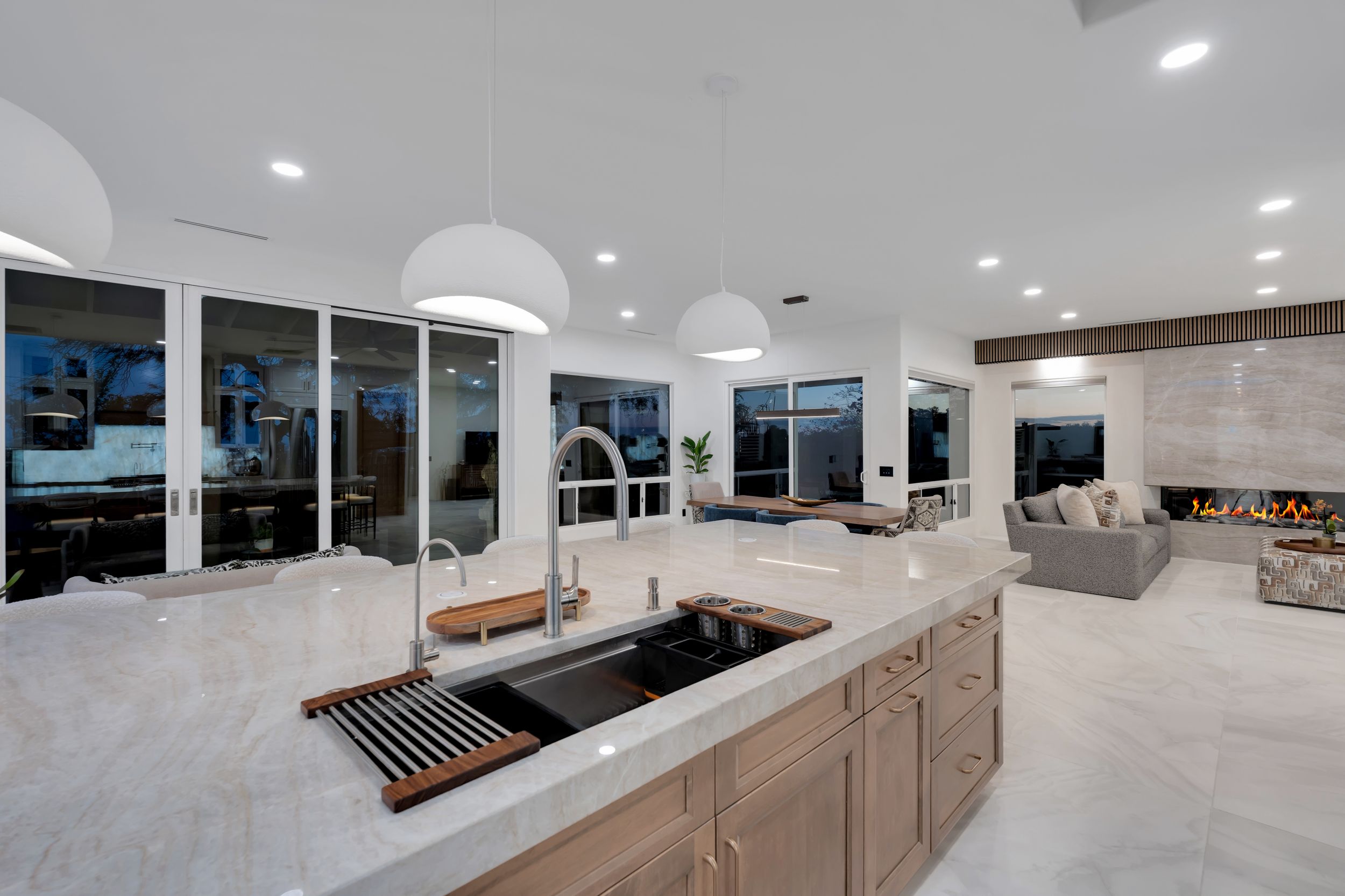 Modern open-concept kitchen with marble island, pendant lights, and a cozy living area with fireplace in the background.