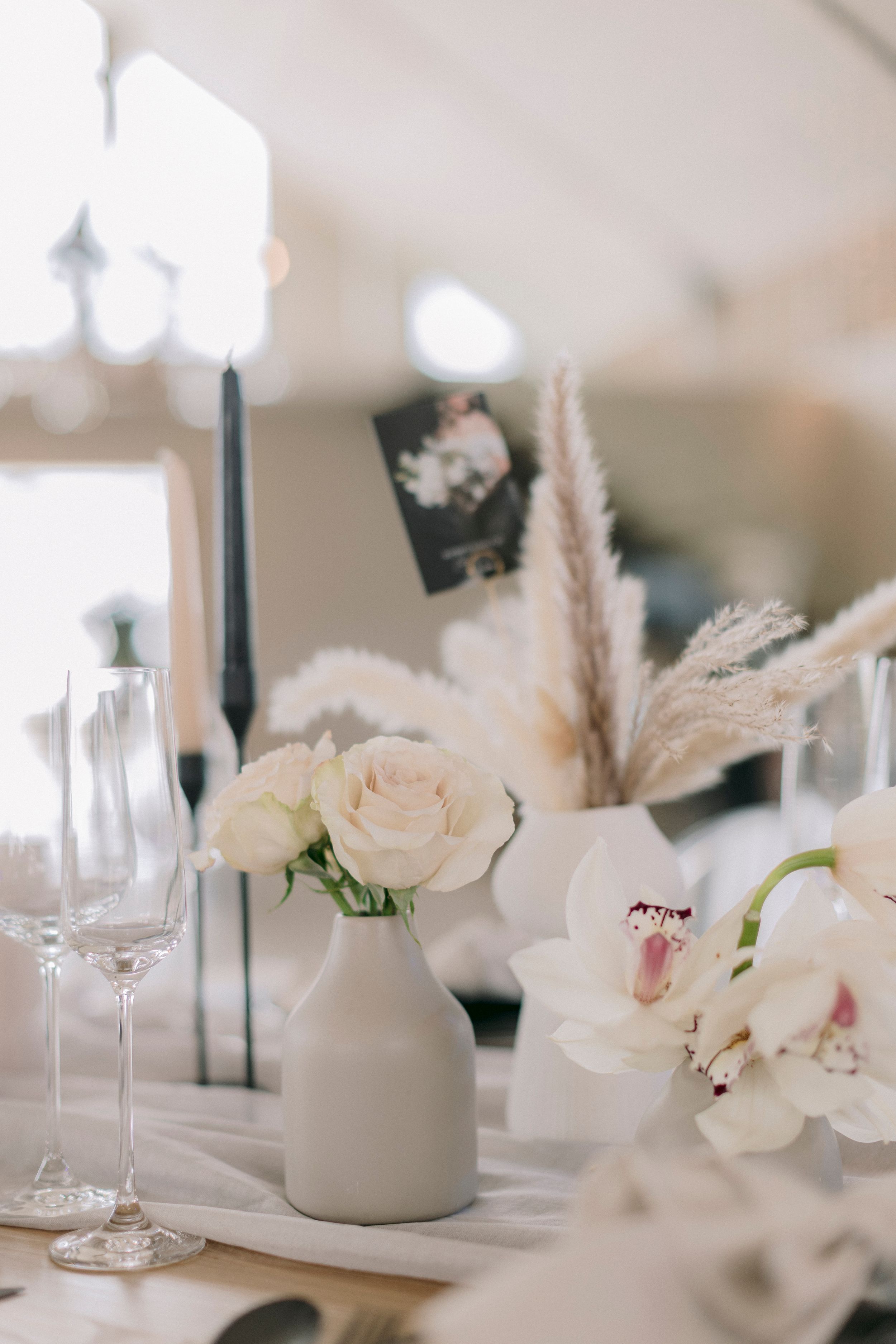 Minimalist wedding table with white roses in a gray vase, black candles, pampas grass, and orchid centerpieces.