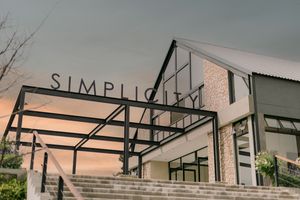 Exterior view of Simplicity venue with modern steel signage, stone walls, and steps at dusk.
