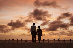 Silhouette of a couple holding hands watching a romantic sunset over the ocean with dramatic orange clouds.