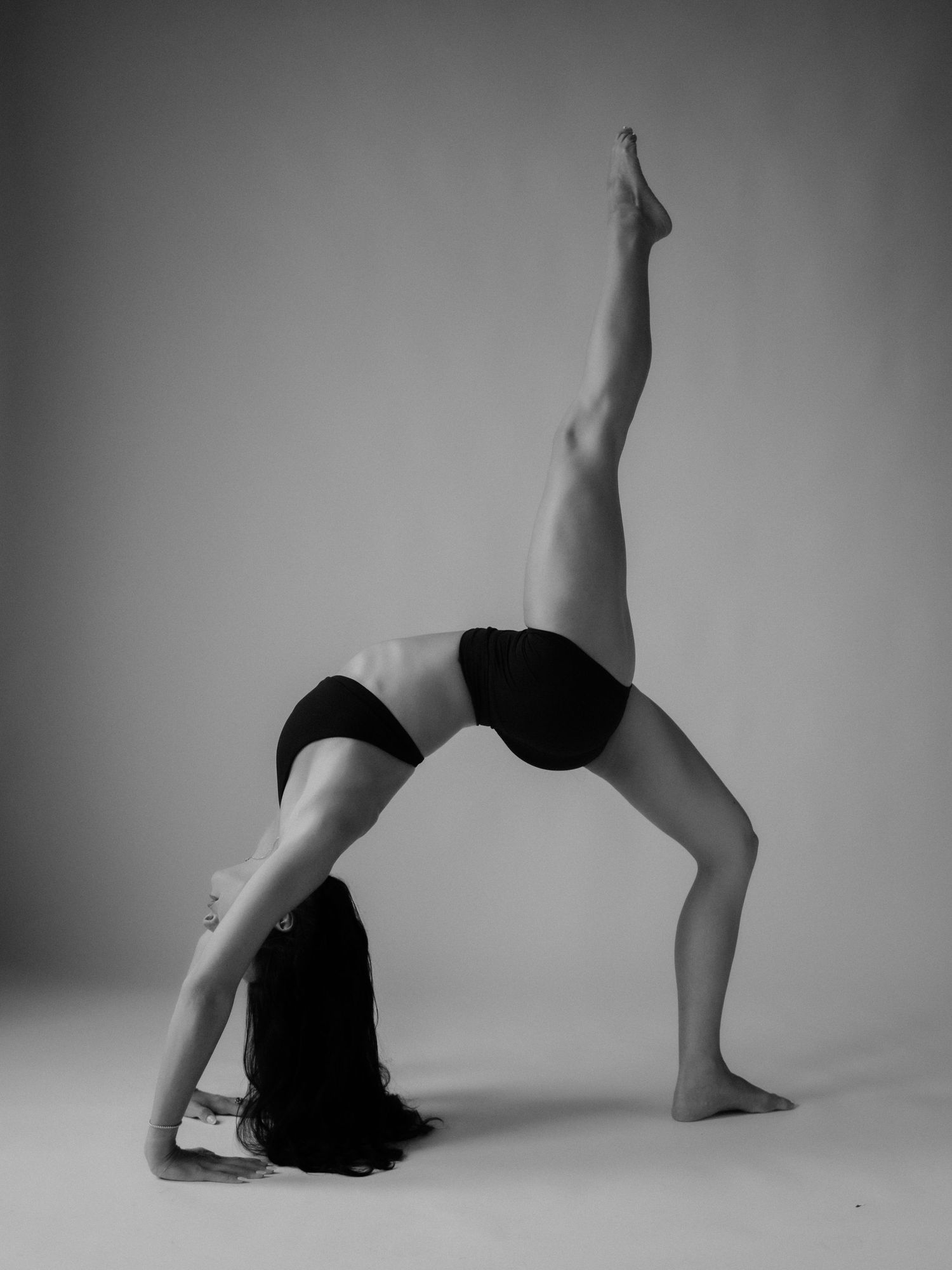 Black and white photo of a woman performing a one-legged wheel yoga pose, showcasing flexibility and strength.