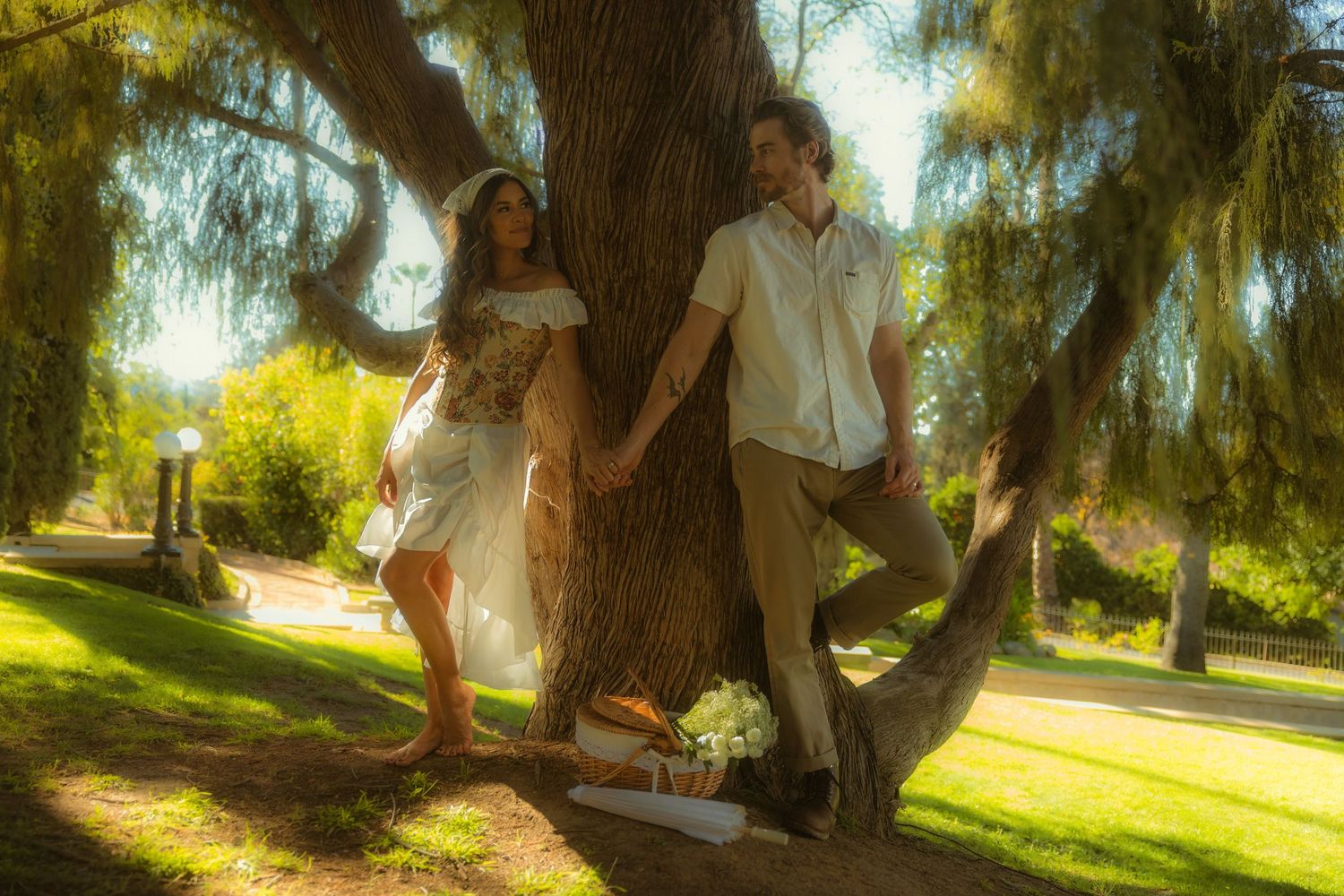 Couple holding hands leaning against a large tree on the grounds of the Kimberly Crest House & Gardens.