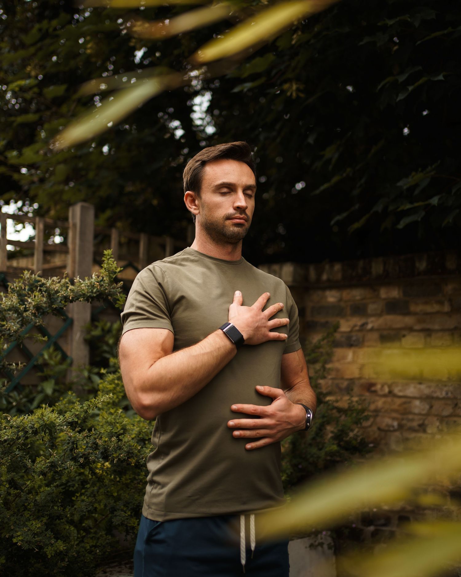 Man in olive green t-shirt jogging outdoors in a park with trees and foliage in the background.