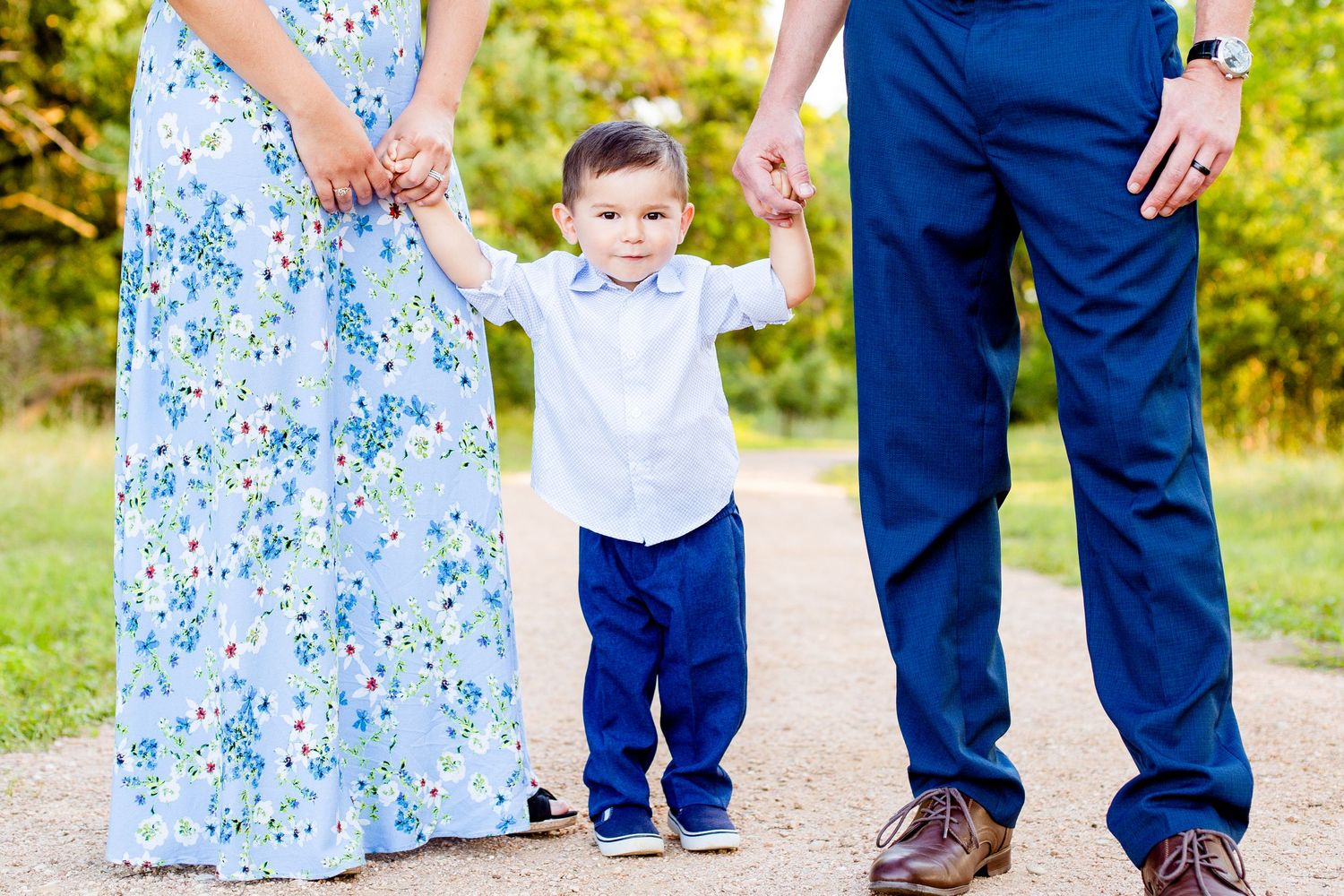 Photo of a four year-old boy holding his mom and dad's hands during golden hour at a park in Seguin Texas.