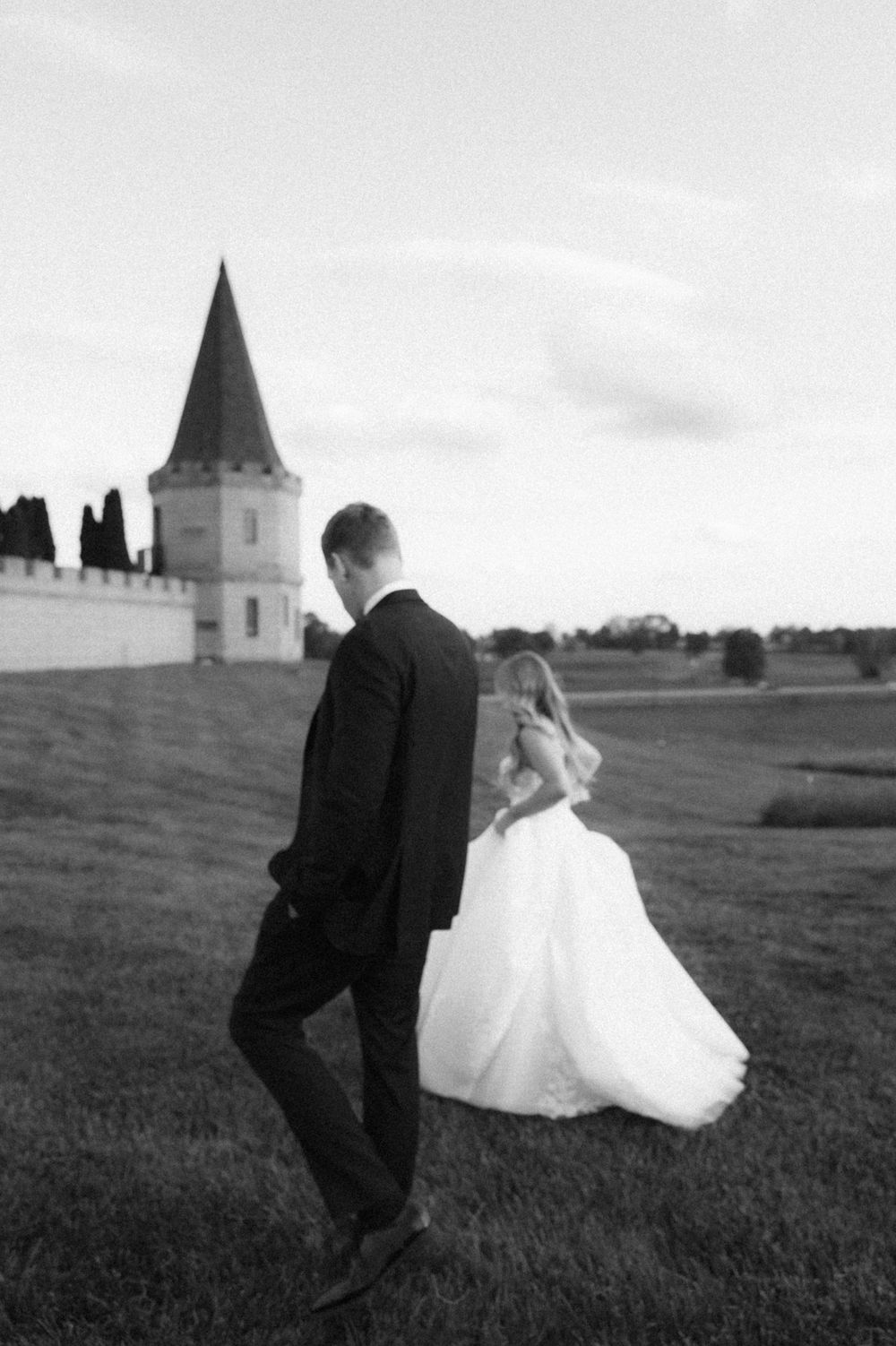 Black and white photo of a bride and groom walking near a castle on their wedding day.